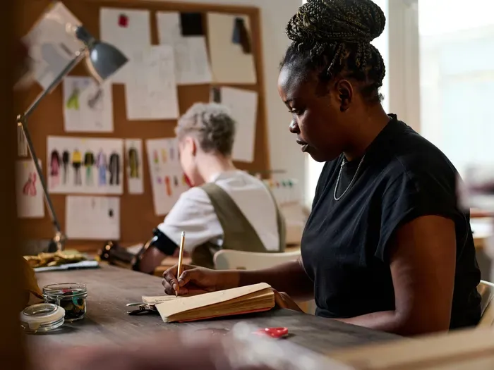 Two designers collaborating in a studio, sketching ideas in notebooks surrounded by art materials